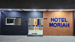 Een hotelentree met een glazen deur, een bord waarop 'HOTEL MORIAH' staat, en het nummer '5495' boven de deur.