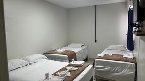 Een hotelkamer met drie eenpersoonsbedden, een wandtelevisie en een plafondlamp.