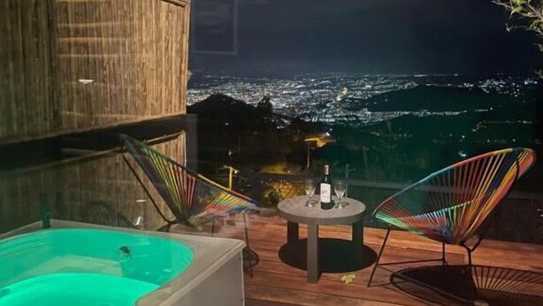A rooftop terrace with a hot tub, two chairs, and a table with a bottle and glasses. - Romero Glamping y Cabañas (Cali)