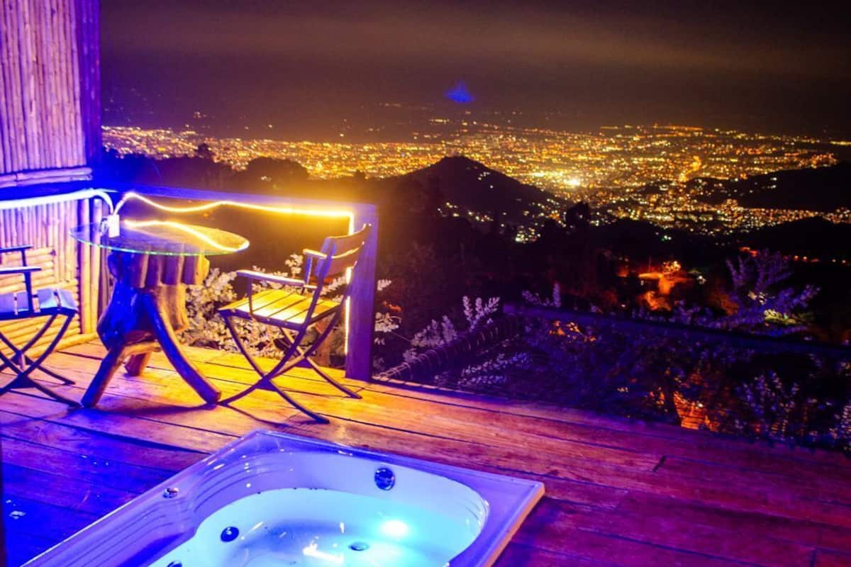 Un jacuzzi en una terraza de madera con vista a la ciudad de noche.