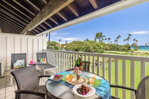 A covered outdoor dining area with a table set for two, overlooking a beach with palm trees. - Kiahuna 216 At Koloa Kai Ocean View  PBAC Access (Koloa)
