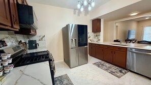 Eine moderne Küche mit einem Edelstahl-Kühlschrank, einem eingebauten Backofen, Marmorarbeitsplatten, Holzschränken und einem Fenster mit Jalousien.
