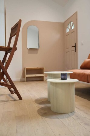 A room with a wooden chair, a small white table, a bench, and a bed with an orange blanket.