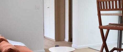 A room with a wooden floor, a round white table, a brown sofa, and a wooden chair.