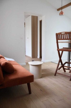 A room with a wooden floor, a round white table, a brown sofa, and a wooden chair. - Dependency on 19 between Paris and Disney (Neuilly-sur-Marne)