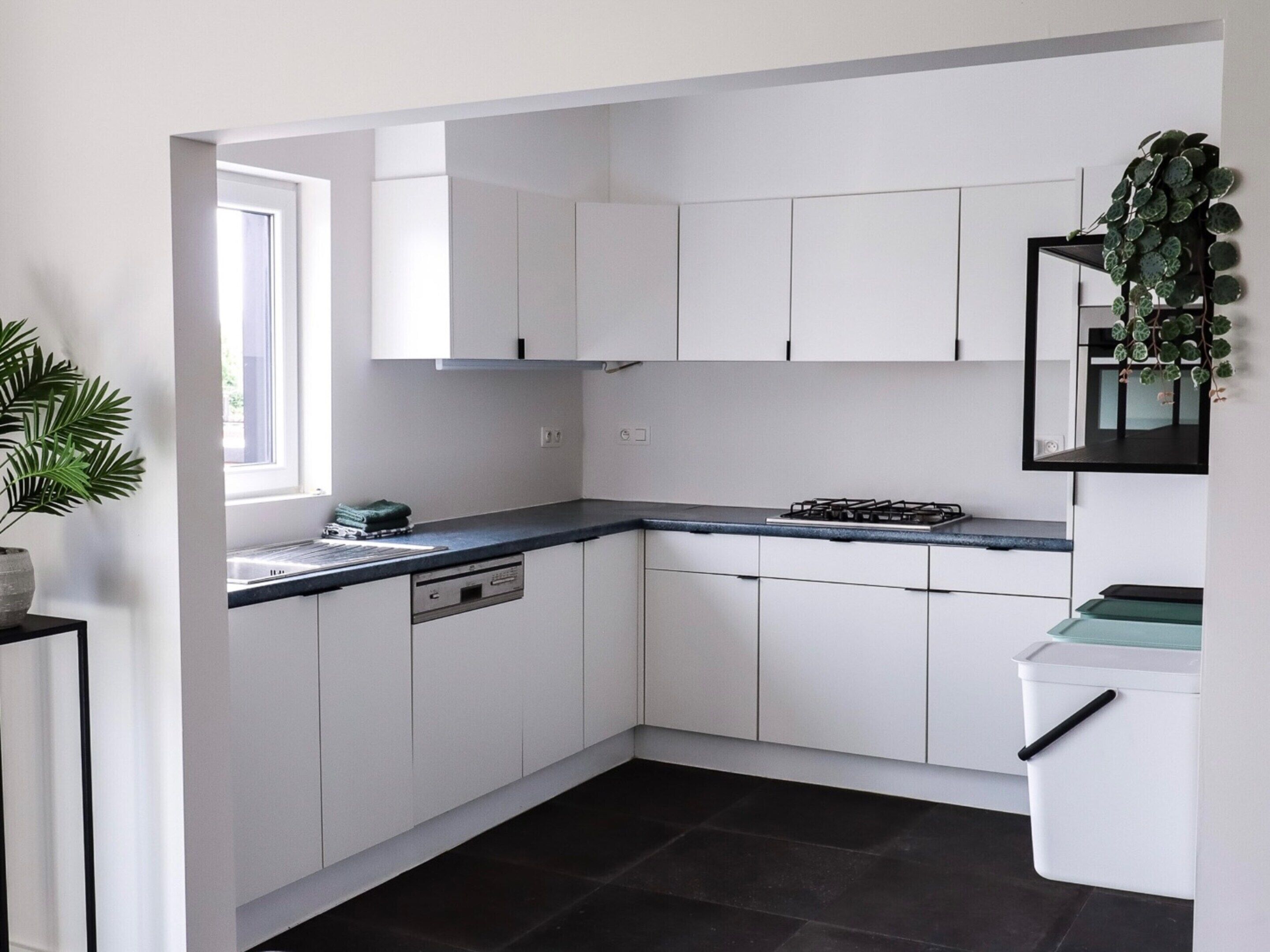 A modern kitchen with white cabinets, a black countertop, and a gas stove.