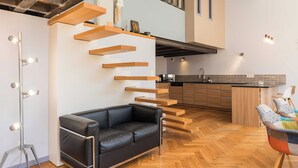 A modern interior with a black leather sofa, wooden floating stairs, a kitchen, and a light-colored floor. - Stunning Apartment - 4br-7p - Crequi (Lyon)