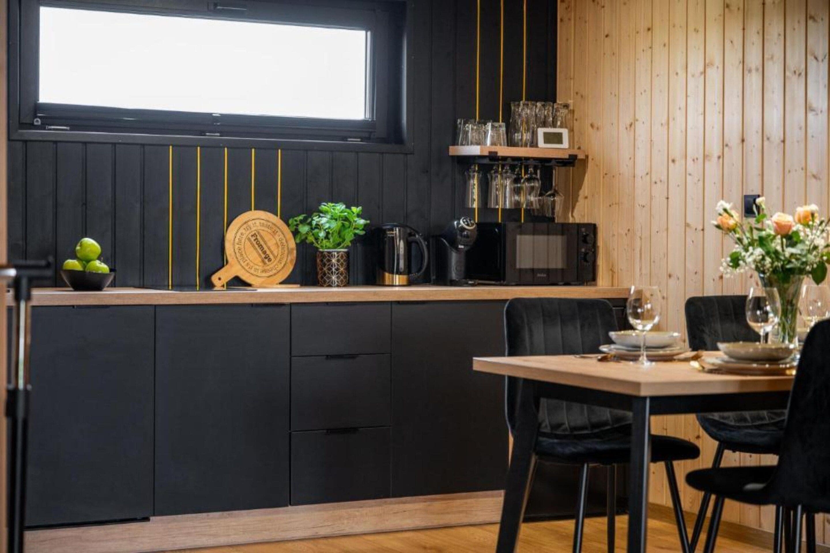 A modern kitchen with a wooden countertop, black cabinets, a coffee machine, and a dining area with a table set for two.