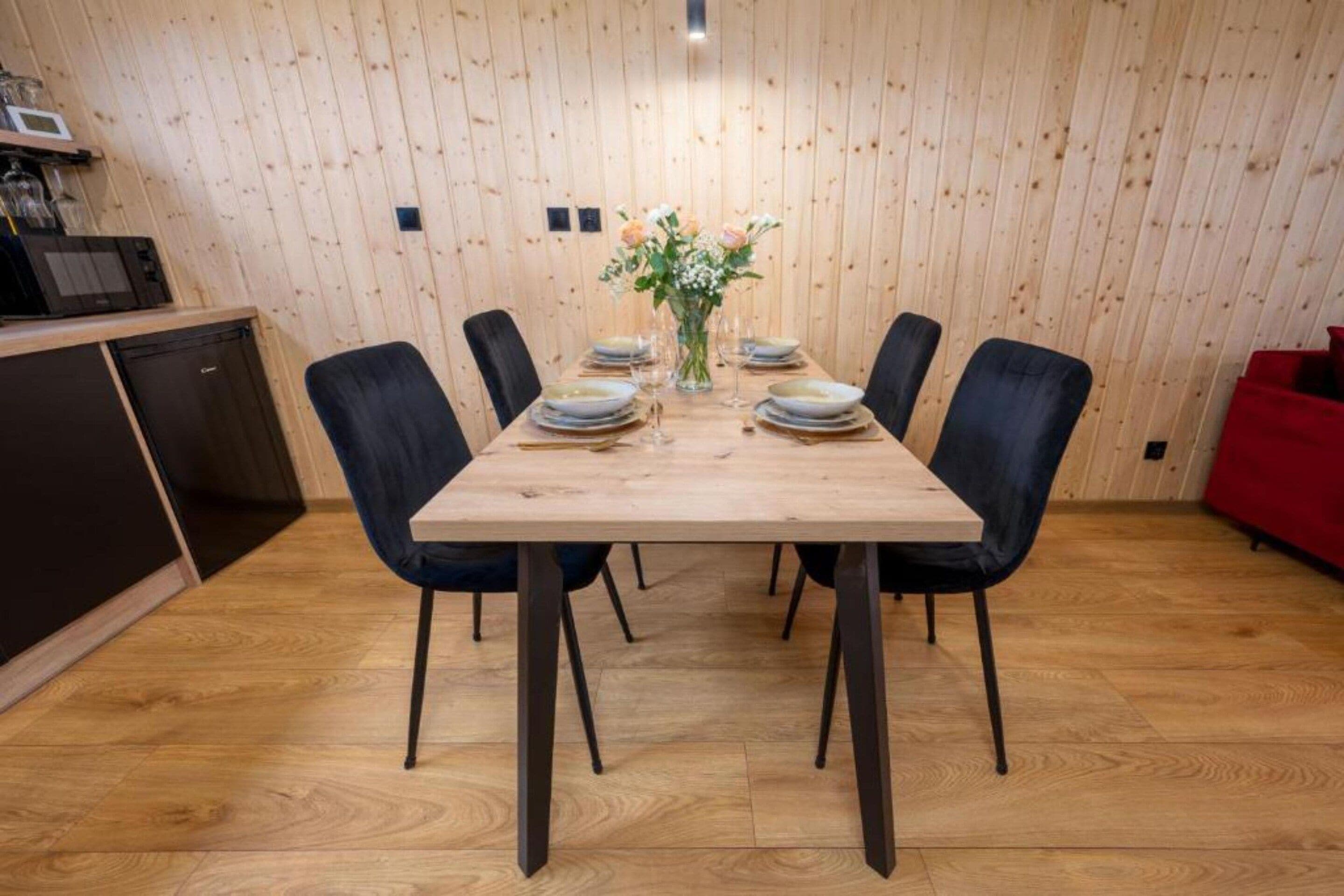 Ein Essbereich mit einem Holztisch, gedeckt für sechs Personen, umgeben von Stühlen, in einem Raum mit Holzwänden und einer roten Couch im Hintergrund.