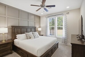 A bedroom with a bed, nightstands, a ceiling fan, a window with curtains, and a TV on a stand. - Tiger Walk Townhouse (Auburn)