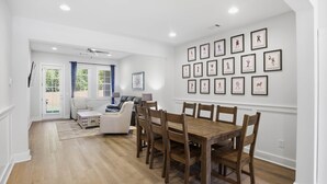 Uma sala de jantar com uma mesa e cadeiras de madeira, um sofá branco e uma parede com quadros.