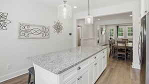 Cozinha com bancadas de granito, armários brancos, iluminação pendente e decoração na parede.