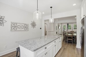 A kitchen with granite countertops, white cabinetry, pendant lighting, and decorative wall art. - Tiger Walk Townhouse (Auburn)