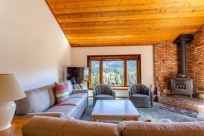 Ein Wohnzimmer mit einer Couch, zwei Sesseln, einem Couchtisch, einem Fernseher und einem Kamin aus Ziegelsteinen.
