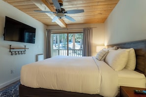 A bedroom with a large bed, a ceiling fan, a mounted TV, and a view of the outdoors. - 2+Loft Canyon Lodge Cabin - Pool/Jacuzzi/Parking! (Mammoth Lakes)