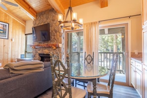 A cozy cabin interior with a stone fireplace, a dining table with chairs, a sofa, and a TV mounted on the wall. - 2+Loft Canyon Lodge Cabin - Pool/Jacuzzi/Parking! (Mammoth Lakes)