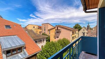 A residential building with a red-tiled roof, a blue balcony railing, and a view of neighboring houses.