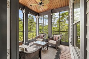 Eine überdachte Terrasse mit Korbmöbeln, großen Fenstern und einem Deckenventilator.