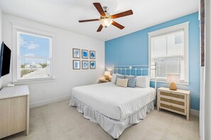 Une chambre à coucher avec un lit, deux tables de chevet, un ventilateur de plafond et un téléviseur.