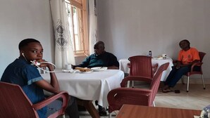 Un comedor con mesas redondas y sillas rojas, una ventana con cortinas, y una mesa con comida y bebidas.