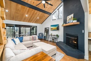 A modern living room with a sectional sofa, a fireplace, and a large window. - All Decked Out Lake House & Dock (Blue Ridge)