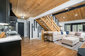 A modern interior with a wooden staircase, a kitchen area, and a living room with a sofa and coffee table. - All Decked Out Lake House & Dock (Blue Ridge)