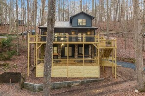 A two-story wooden cabin with a balcony, surrounded by trees. - All Decked Out Lake House & Dock (Blue Ridge)
