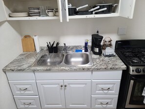 Una cocina con encimera de granito, pileta de acero inoxidable, gabinetes blancos, estufa y microondas.