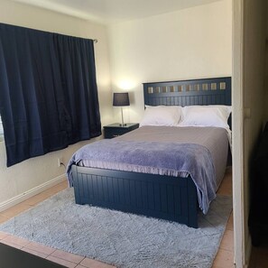 A bedroom with a bed, nightstand, lamp, and a window with curtains.