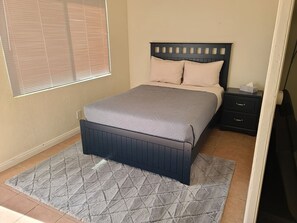 A bedroom with a bed, a nightstand, a window with blinds, and a patterned rug.