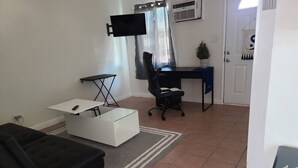 A living room with a black sofa, a white coffee table, a black office chair, a desk, and a TV mounted on the wall. - Cozy Cove #6 (Apple Valley)