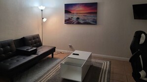A living room with a sofa, a coffee table, a lamp, a TV, and a painting on the wall. - Cozy Cove #6 (Apple Valley)
