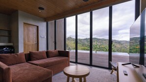Une chambre moderne avec un canapé, une table ronde et une grande fenêtre donnant sur des collines.