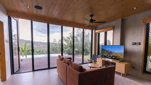 Un salon moderne doté d’une grande porte-fenêtre coulissante, d’un canapé marron, d’un téléviseur à écran plat et d’un ventilateur de plafond en bois.