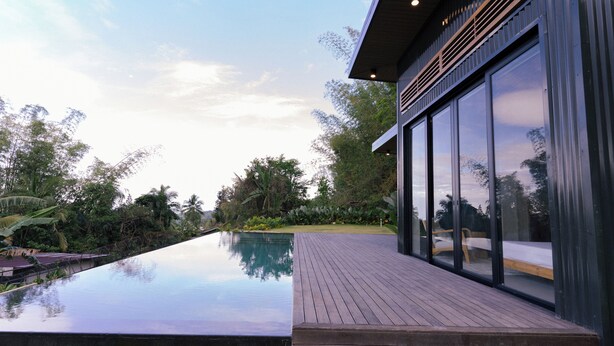 Une maison moderne dotée d’une piscine, de grandes fenêtres et d’une terrasse en bois.