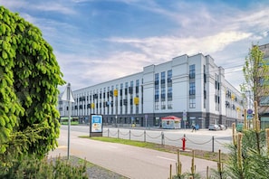 A modern building with a flat facade, large windows, and a paved area with a fence in front.