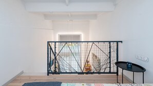 A room with a high ceiling, a black metal gate, a small table with a blue object, and a patterned rug. - Sunshine Loft by Polo Apartments (Kaunas)