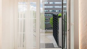 A modern room with a large sliding glass door leading to an outdoor balcony, a grey sofa, and a white curtain. - Sunshine Loft by Polo Apartments (Kaunas)