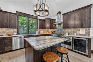 Una cocina moderna con armarios de madera oscura, una isla grande con taburetes, una estufa de acero inoxidable y una lámpara colgante.