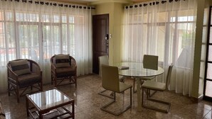 Une pièce avec une table en verre entourée de chaises, un ventilateur de plafond et de grandes fenêtres ornées de rideaux légers.