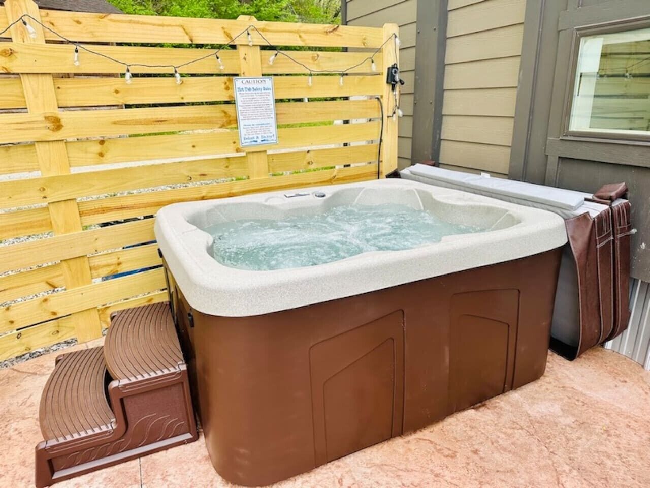 Een hottub met treden, een houten omheining en een waarschuwingsbord.