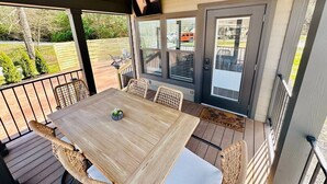 Une terrasse couverte avec une table en bois et des chaises en osier, un ventilateur de plafond et une vue sur l’extérieur.