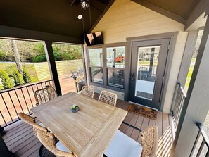 Eine überdachte Terrasse mit einem Holztisch, Korbstühlen, einem Deckenventilator und Blick ins Freie.