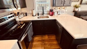 Une cuisine compacte dotée d’une cuisinière intégrée, d’un évier et de meubles de rangement aux couleurs sombres.