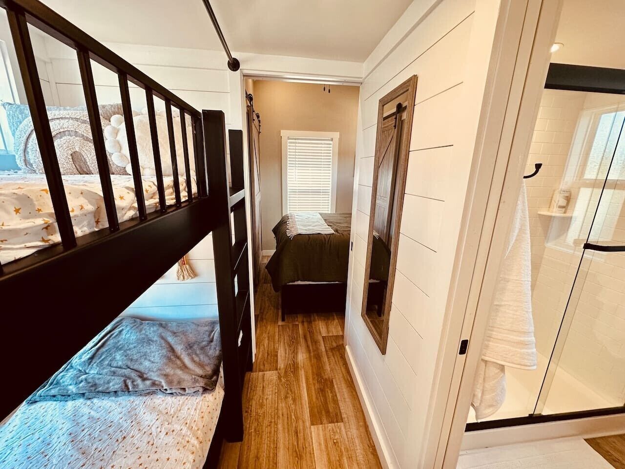 A narrow hallway with a bunk bed, a small bed, and a glass shower enclosure.
