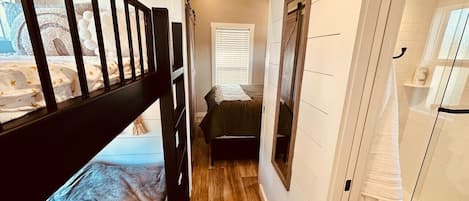 A narrow hallway with a bunk bed, a small bed, and a glass shower enclosure.