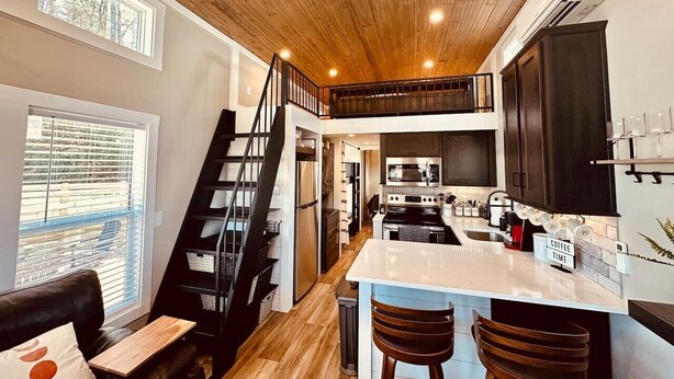 Une cuisine moderne dotée d’un îlot central, d’un escalier menant à un niveau supérieur et offrant une vue sur l’extérieur grâce à une fenêtre.