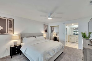 Ein modernes Schlafzimmer mit Bett, Nachttischen, Deckenventilator und Blick ins Bad.