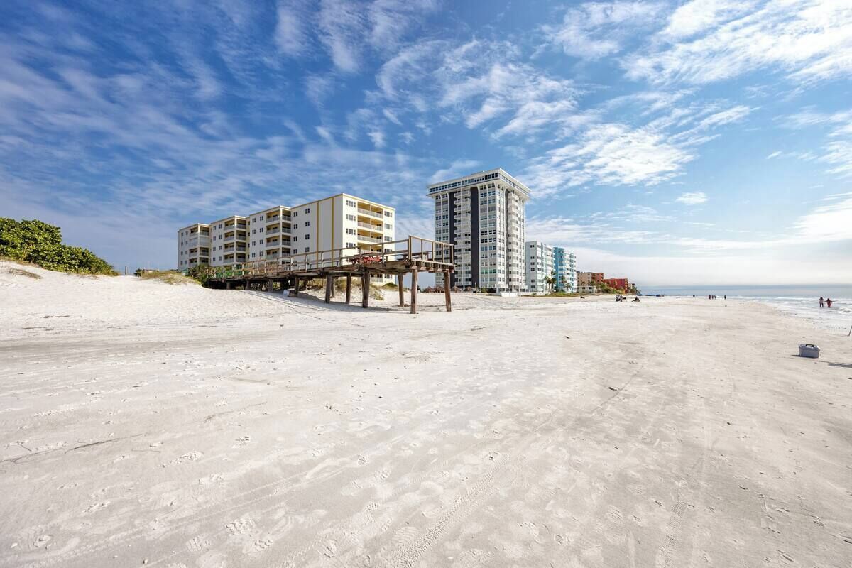 Ein Strand mit einem mehrstöckigen Hotel, einer Pier und blauem Himmel.