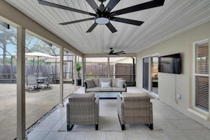 Ein überdachter Patio-Bereich mit Deckenventilatoren, Gartenmöbeln und einem an der Wand befestigten Fernseher.